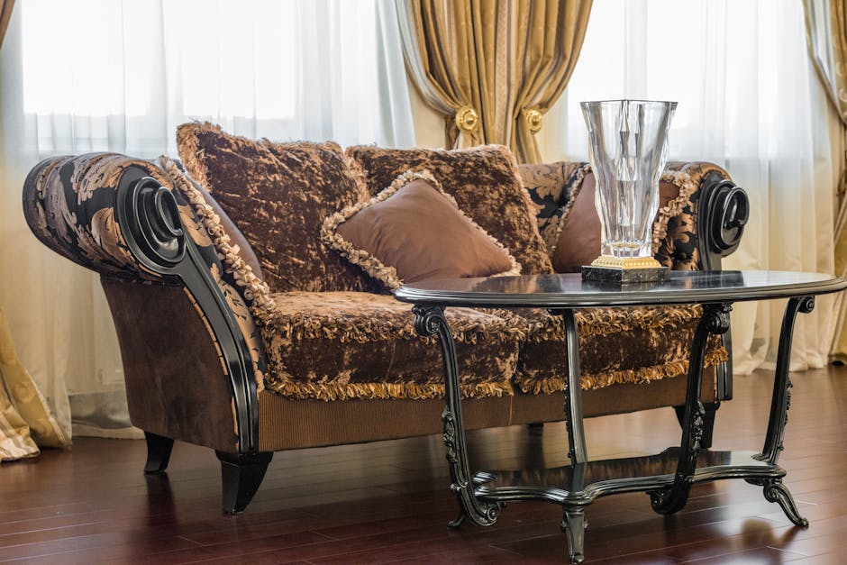 An ornate Victorian-style armchair with a gilded wooden frame and elaborate carvings, upholstered in vibrant pink damask fabric, positioned on a richly patterned oriental rug in a luxurious room. Behi